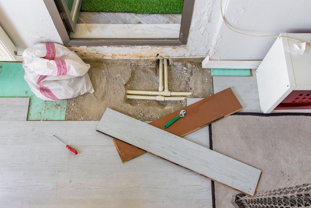 Exposed water pipes under removed laminate flooring during plumbing repair in apartment.